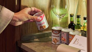 A hand holding a can of Anacardos, with a wine glass and bottles on a counter.