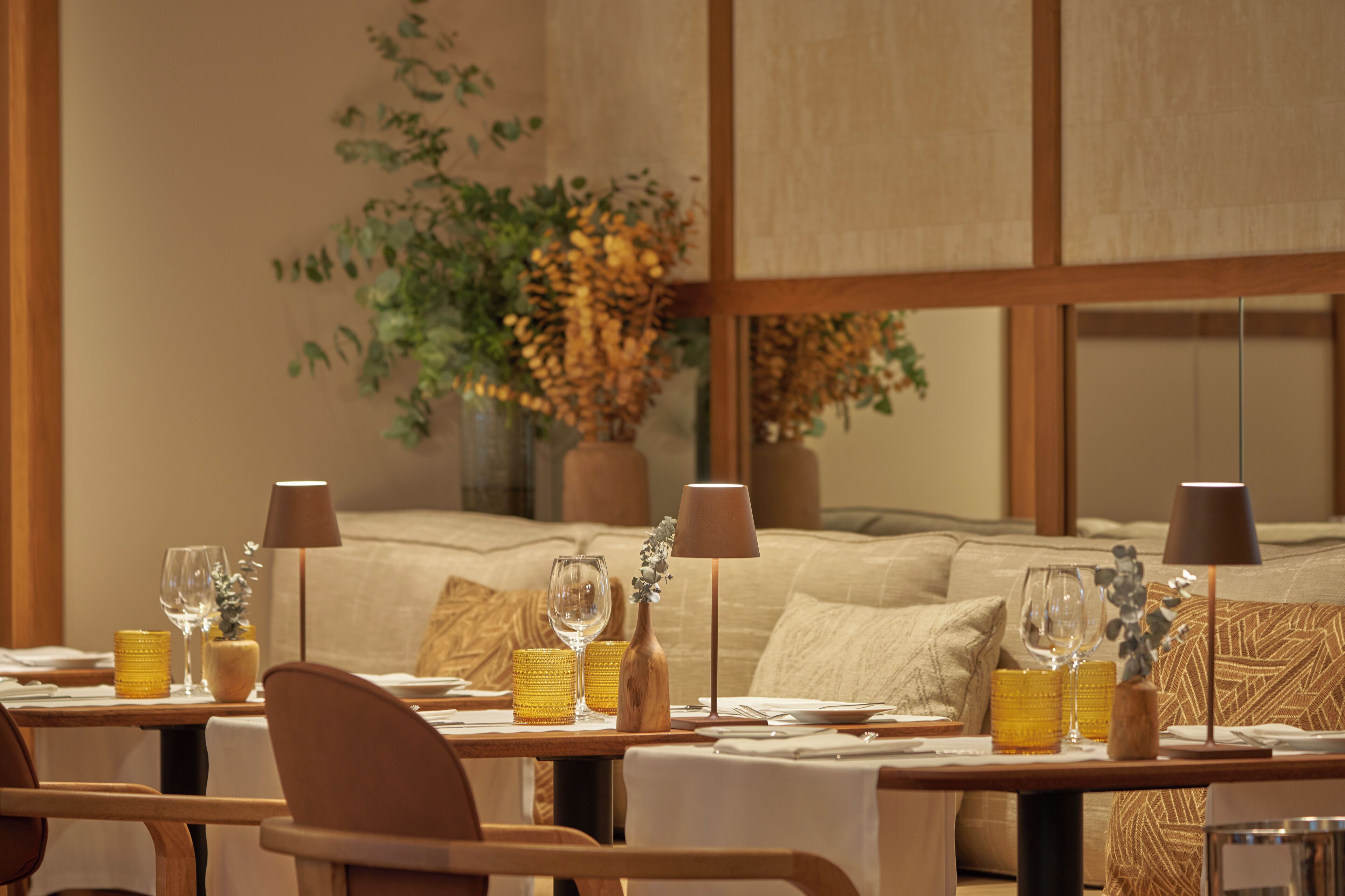 A dining area with tables set for two, featuring yellow candle holders and wine glasses.