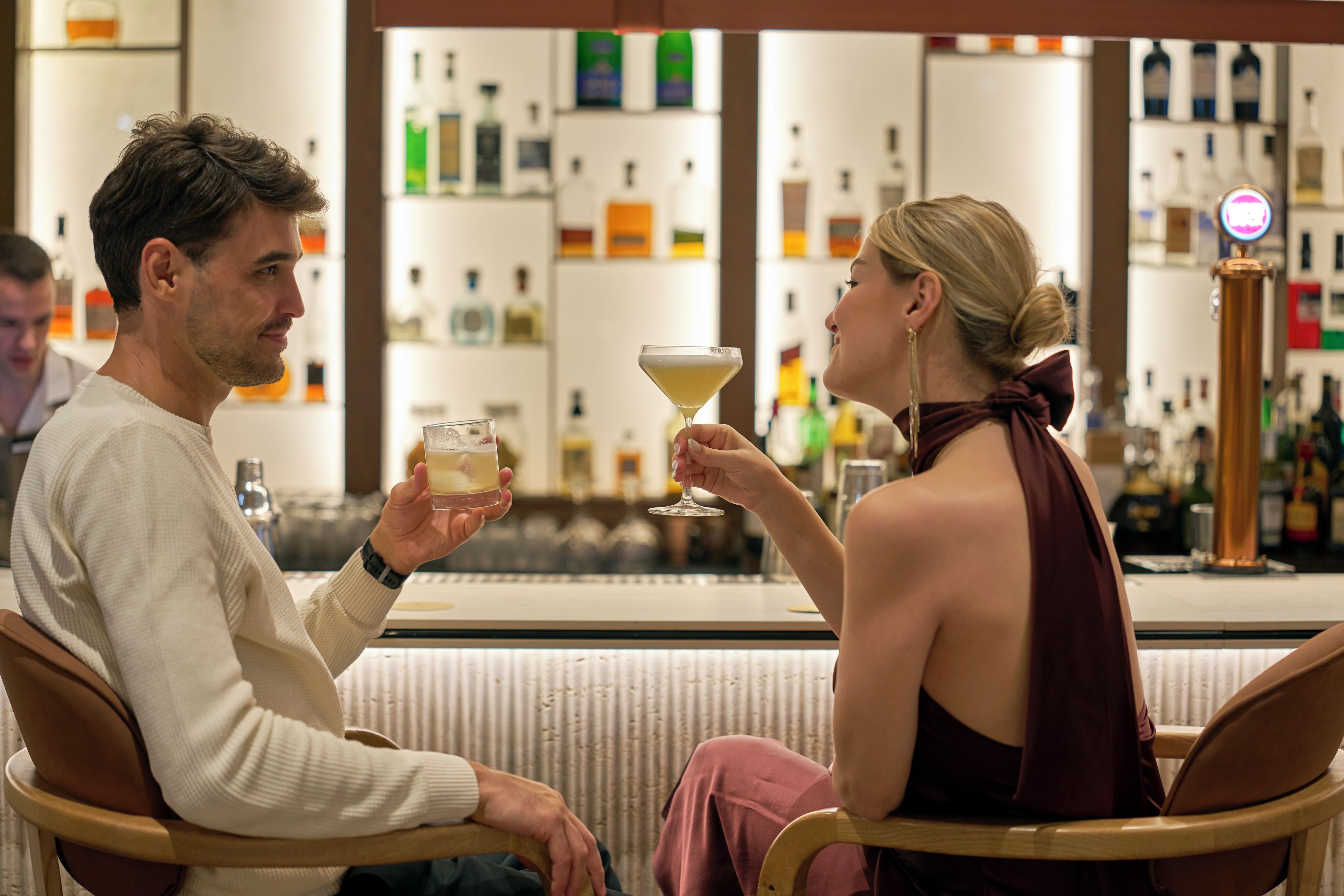Duas pessoas sentadas num bar, com várias garrafas ao fundo.