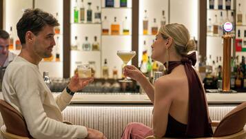 Duas pessoas sentadas num bar, com várias garrafas ao fundo.