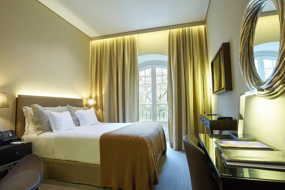 Habitación de hotel con cama, mesita de noche, escritorio, silla y un espejo grande.