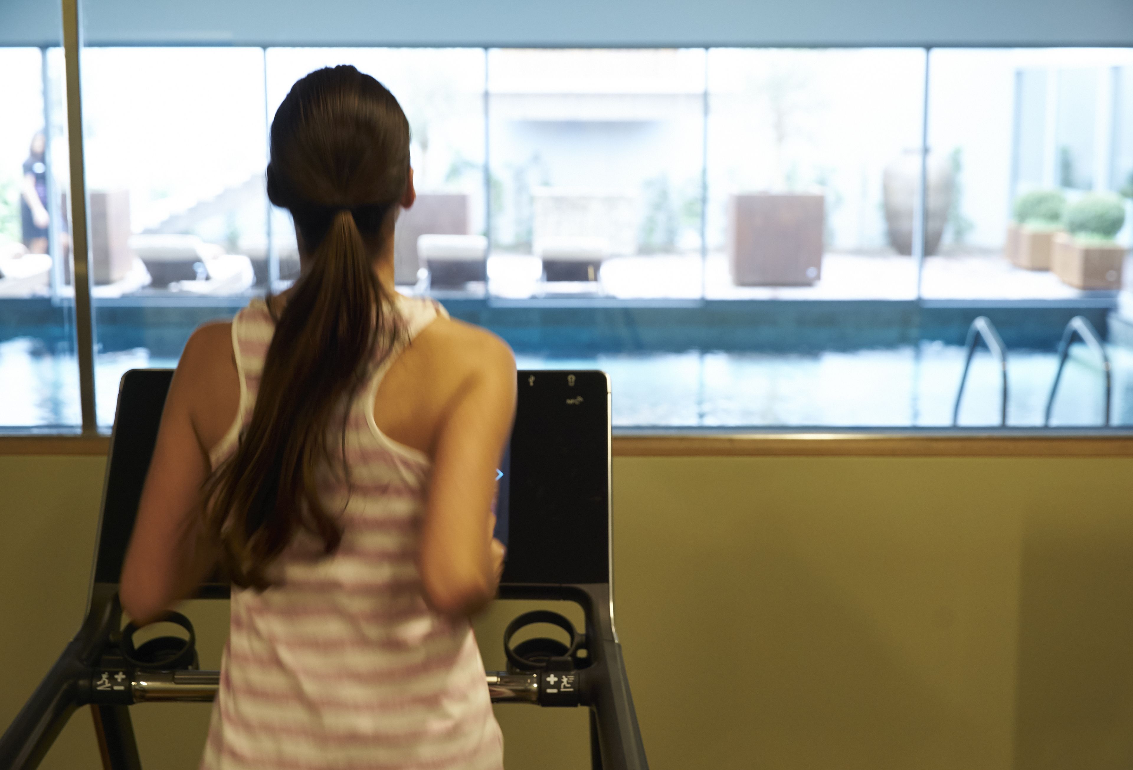 A person using a stationary bike in a room with a large window overlooking a pool area.