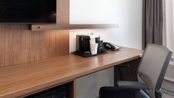 A hotel room with a wooden desk, a coffee maker, a telephone, and a television.