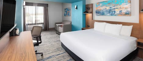 A hotel room with a large bed, a desk, a chair, a TV, and a painting on the wall.