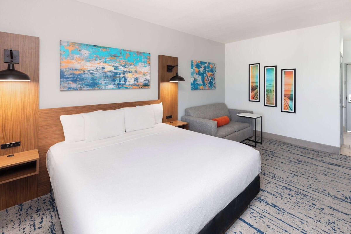 Une chambre d’hôtel avec un grand lit, un bureau, une chaise et des œuvres d’art accrochées aux murs.