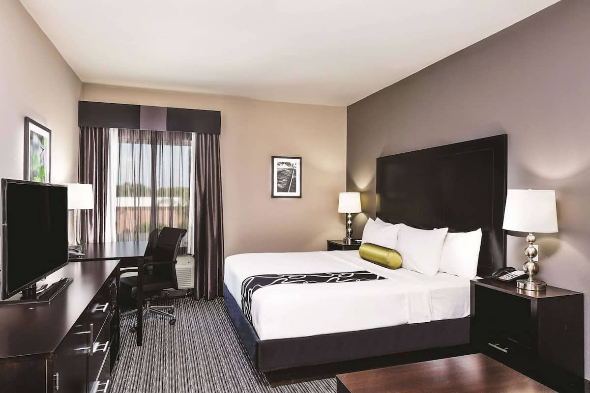 Une chambre d’hôtel avec un lit, un bureau, une télévision et une fenêtre avec des rideaux.