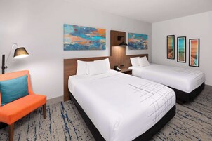 Quarto de hotel com duas camas, uma mesa, uma cadeira e obras de arte nas paredes.