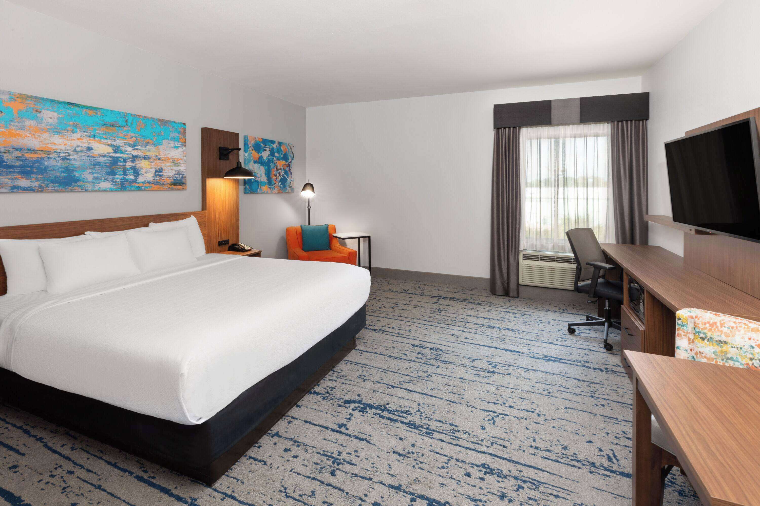 Habitación de hotel con una cama grande, un escritorio, una silla, un televisor y una ventana con cortinas.