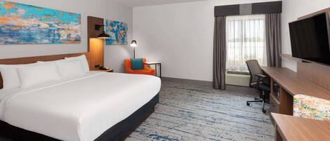 Habitación de hotel con una cama grande, un escritorio, una silla, un televisor y una ventana con cortinas.