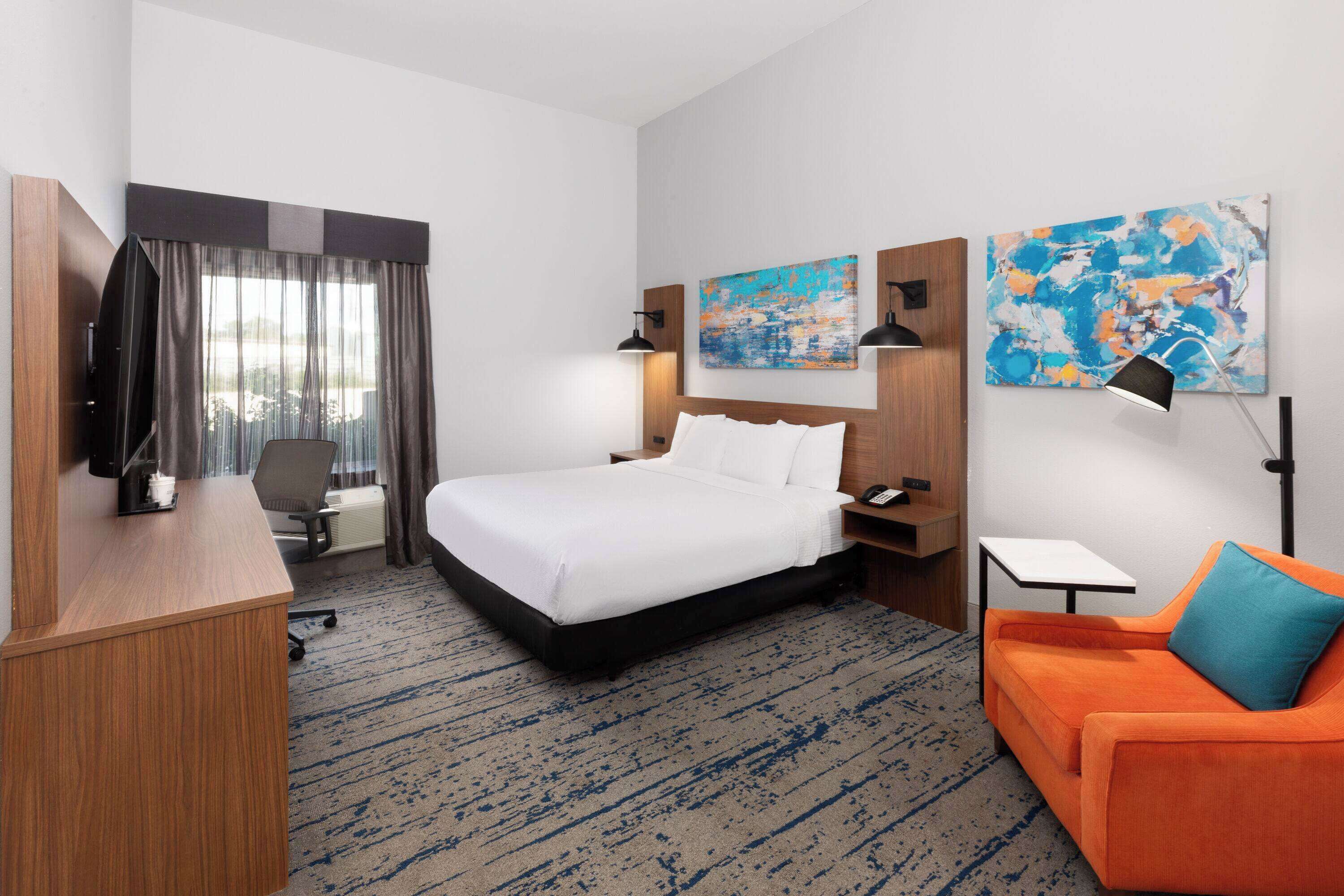 A hotel room with a bed, a desk, a chair, a sofa, and artwork on the walls.