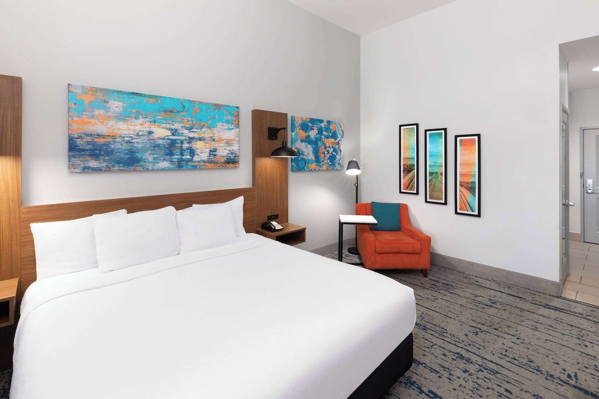 Une chambre d’hôtel avec un grand lit, une table de chevet, un bureau, une chaise et trois tableaux encadrés accrochés au mur.