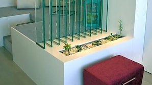 A modern interior with a white reception desk, a red cushioned bench, and a glass partition with vertical bars. - Costa Verde (Povoa De Varzim)