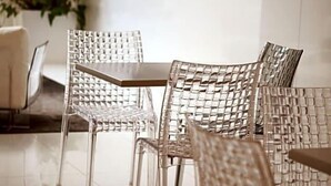 A dining area with clear chairs and a table, a potted plant, and a wall-mounted television. - Costa Verde (Povoa De Varzim)