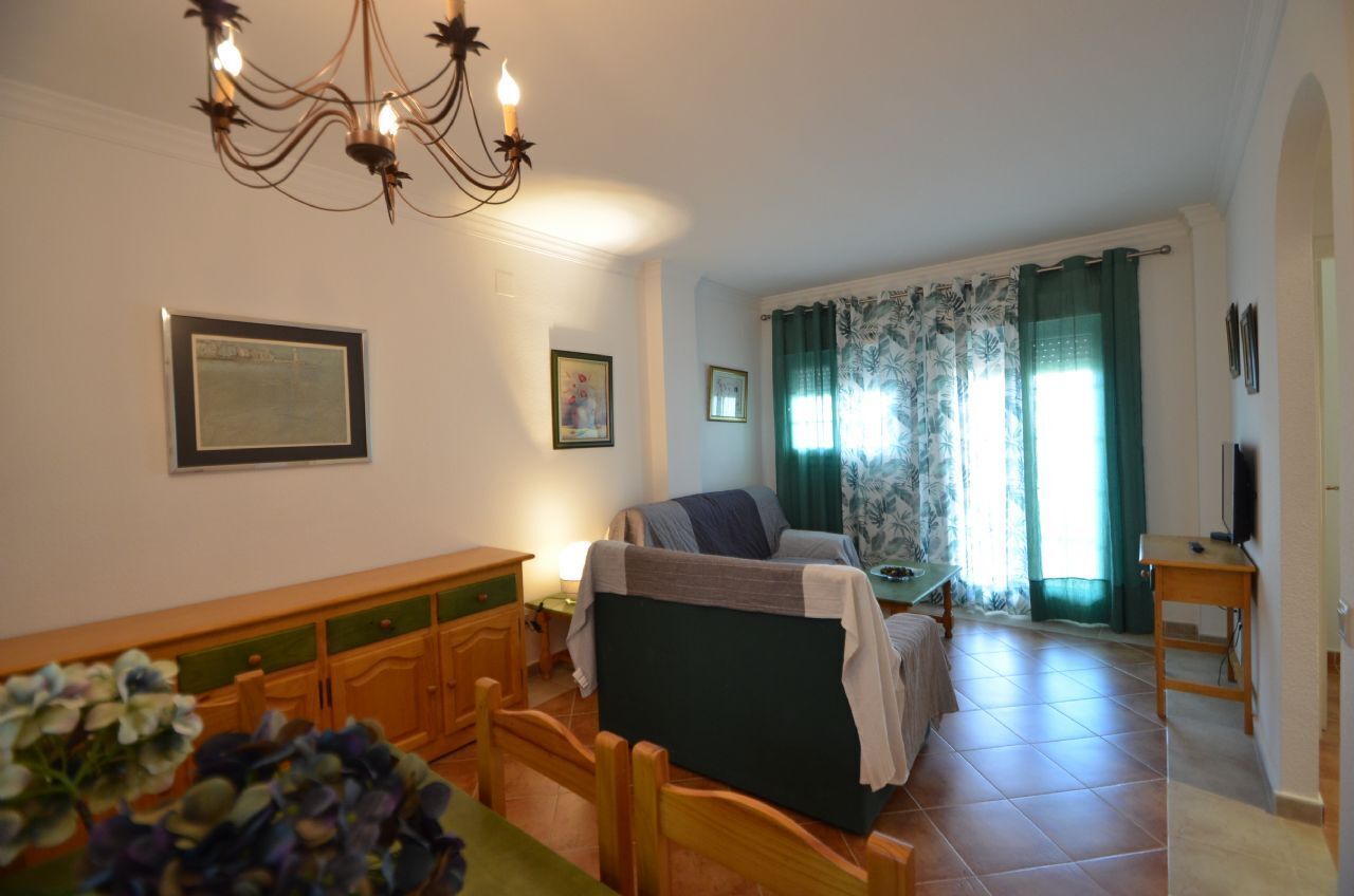 A room with a bed, a desk, a chair, a table, a chandelier, and a window with curtains.