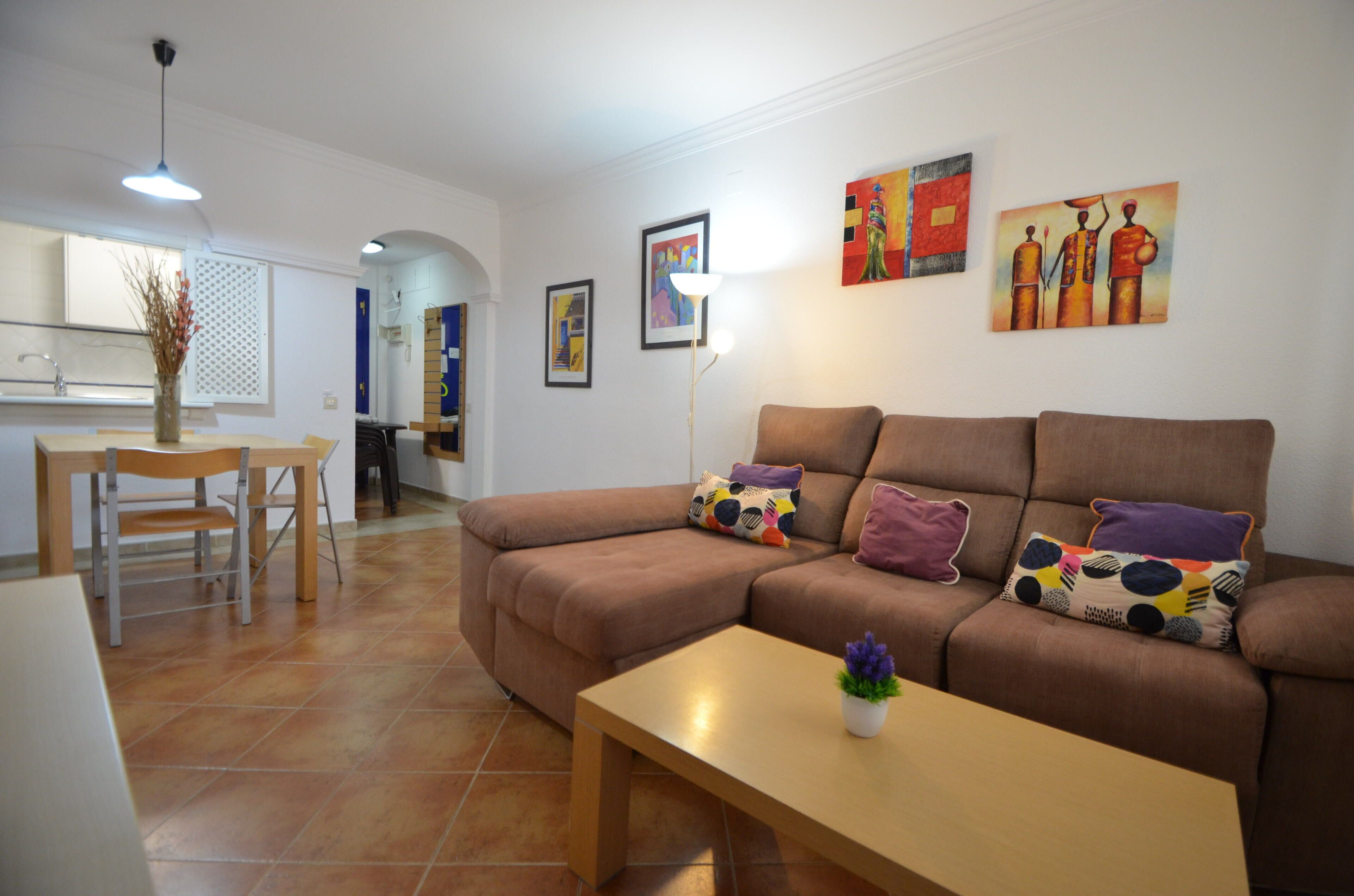 A living room with a brown sofa, a wooden coffee table, and a dining area with a table and chairs.