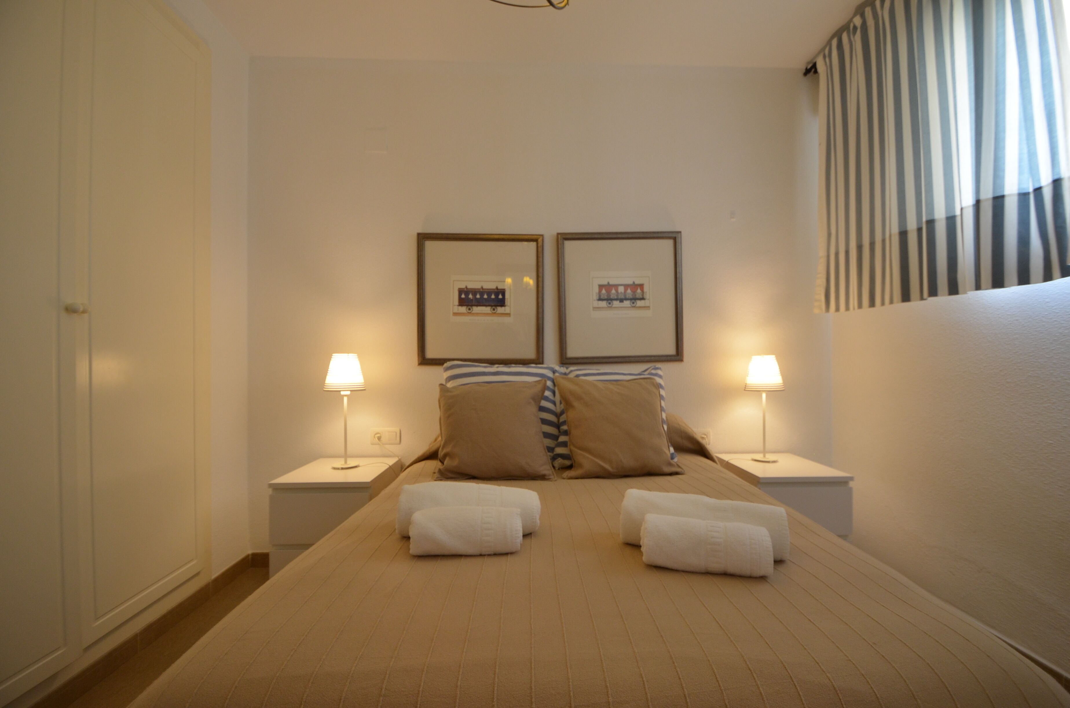 A hotel room with a large bed, two bedside tables with lamps, and two framed pictures on the wall.
