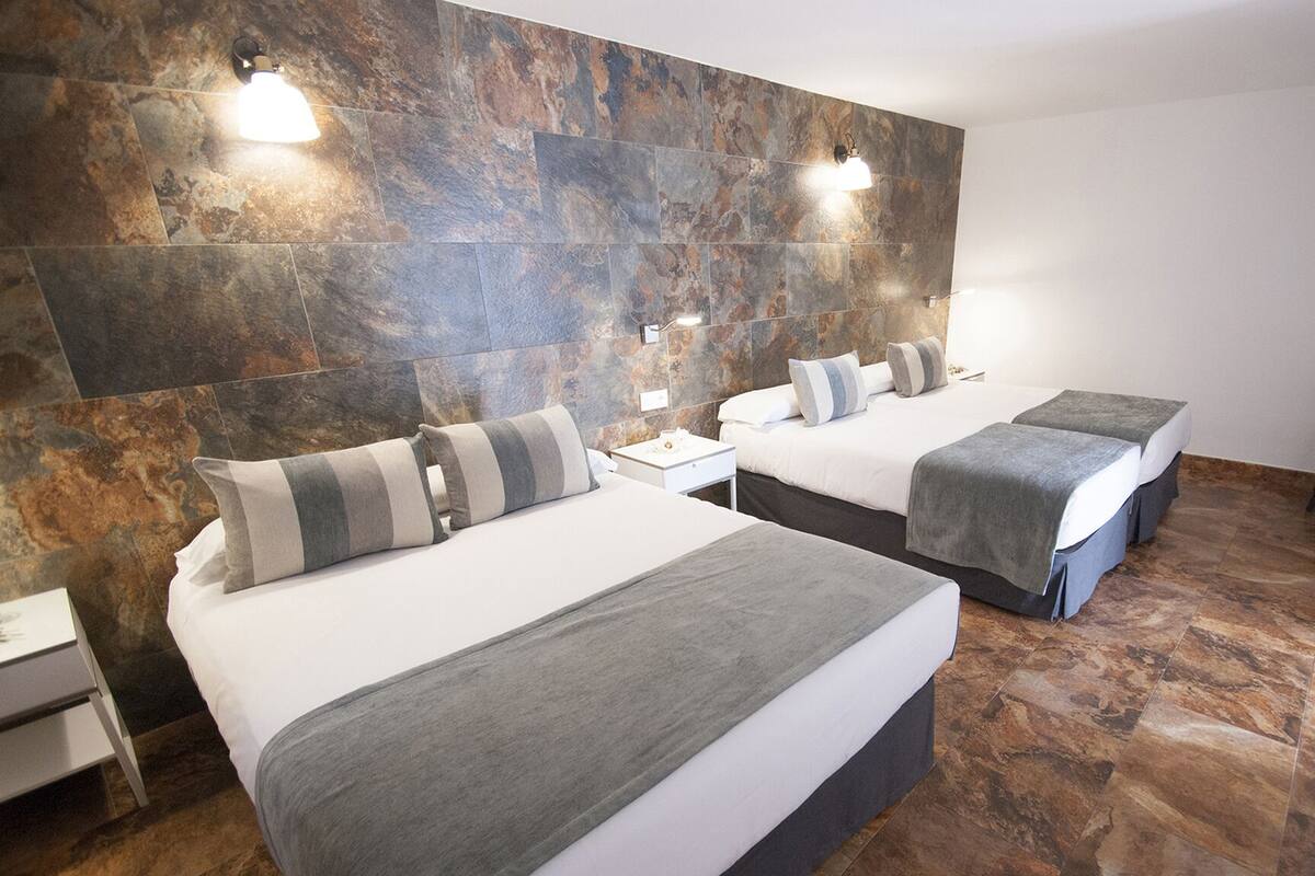 Ein Hotelzimmer mit zwei Betten, einer Steinwand und einem kleinen Tisch mit Stühlen.