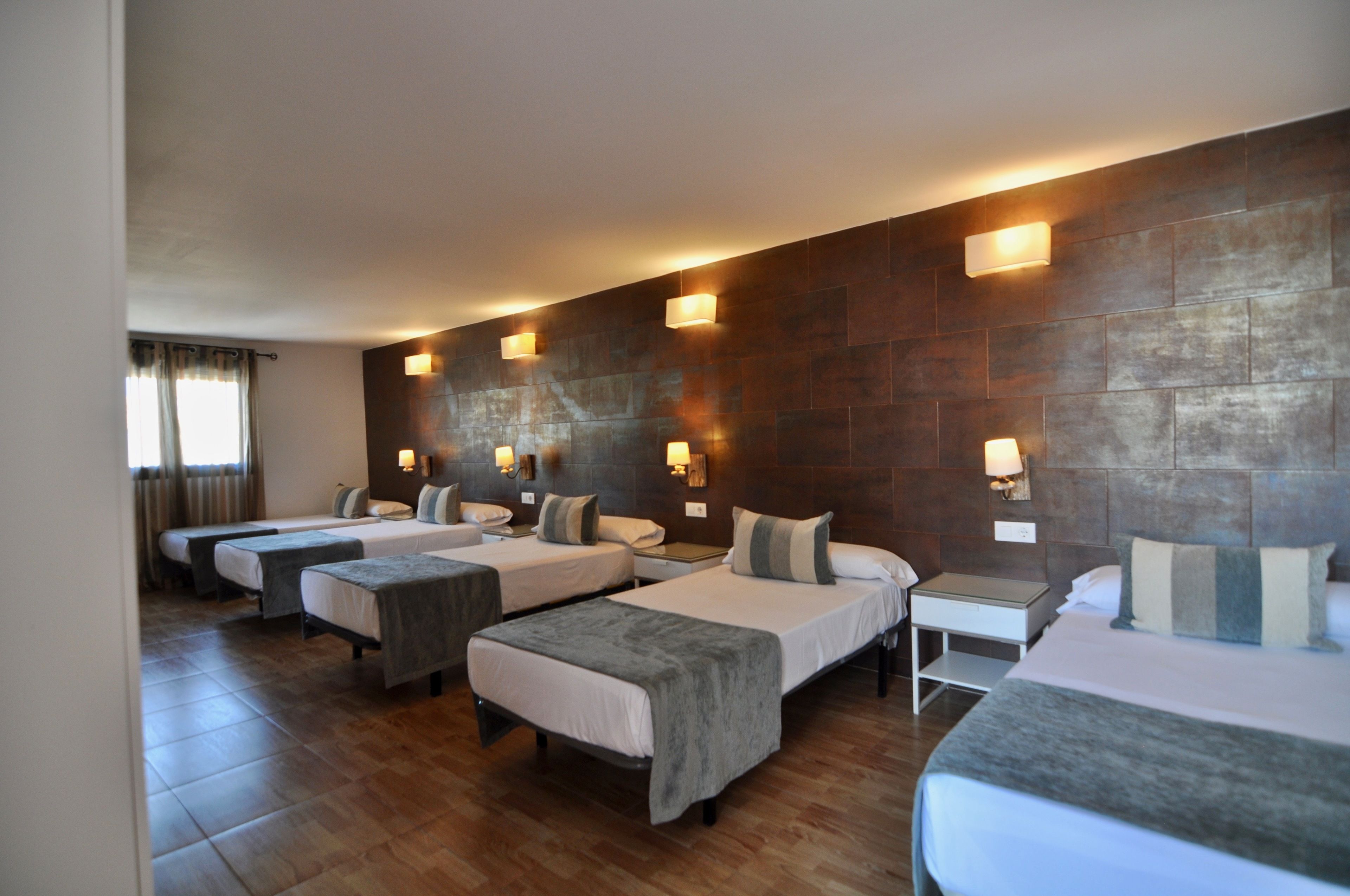A hotel room with four single beds, a small bedside table, and a large wall-mounted TV.