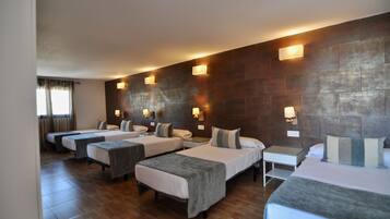 A hotel room with four single beds, a small bedside table, and a large wall-mounted TV.