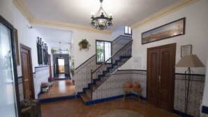 Ein geräumiger Flur mit Fliesenboden, einer Treppe mit blau-weißen Ziergittern und einer Chandelier.