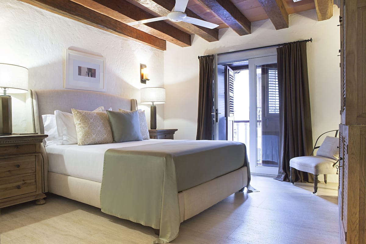 Un dormitorio con cama, mesitas de noche, una silla y vistas al exterior.