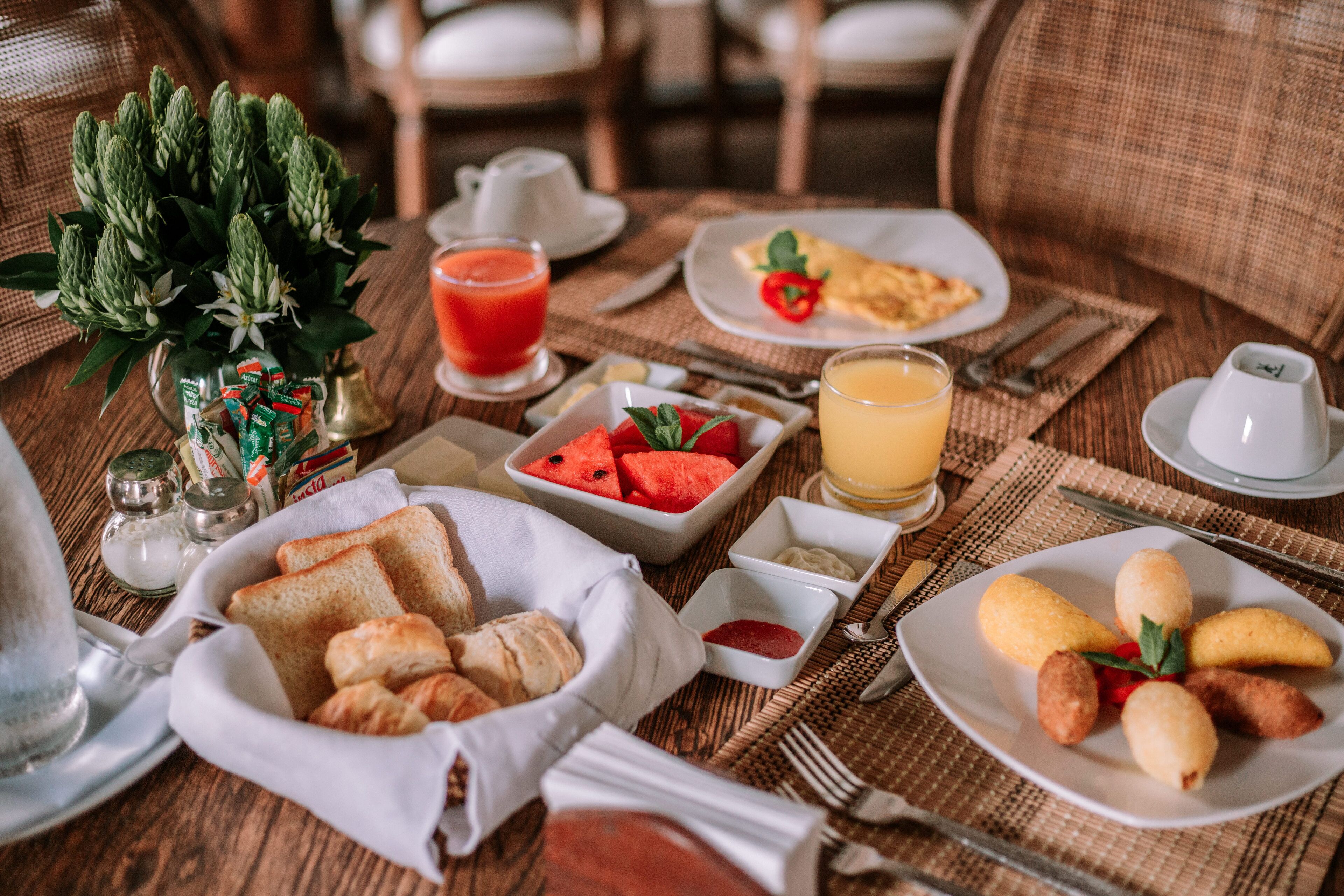 A breakfast setting with toast, croissants, watermelon, orange juice, and a plate of eggs.