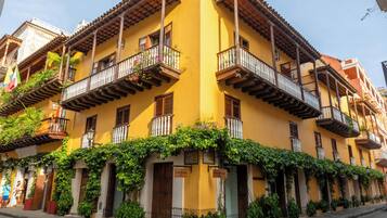 Um edifício amarelo com varandas, plantas em vasos e vista para a rua.