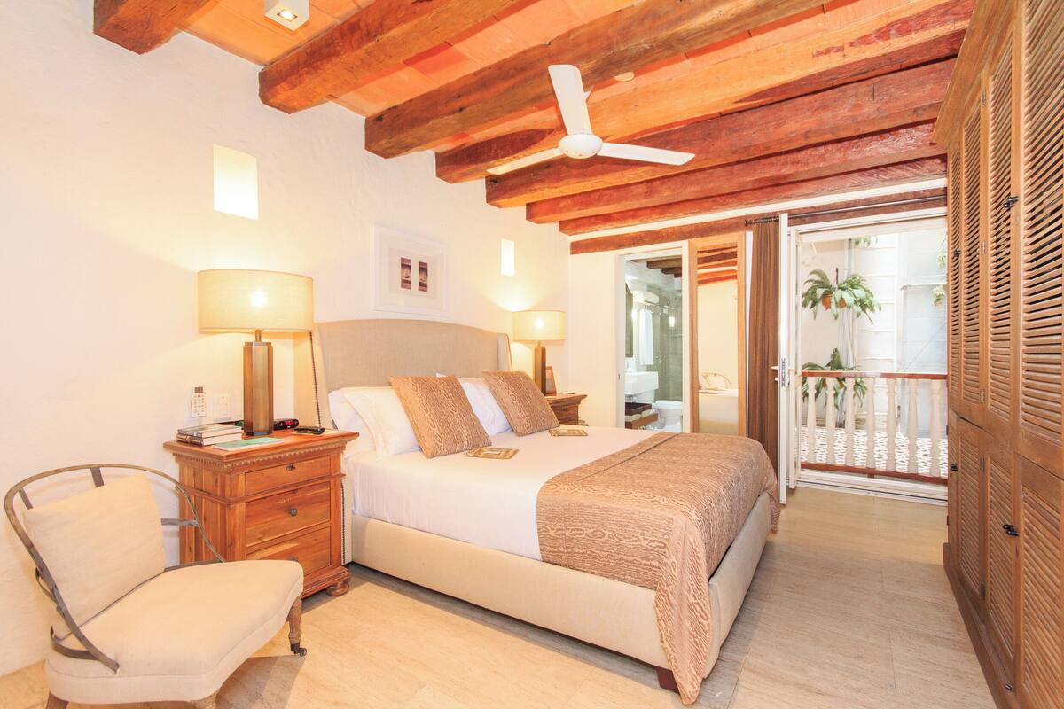Un dormitorio con cama, mesitas de noche, una silla, ventilador de techo y vista al balcón exterior.