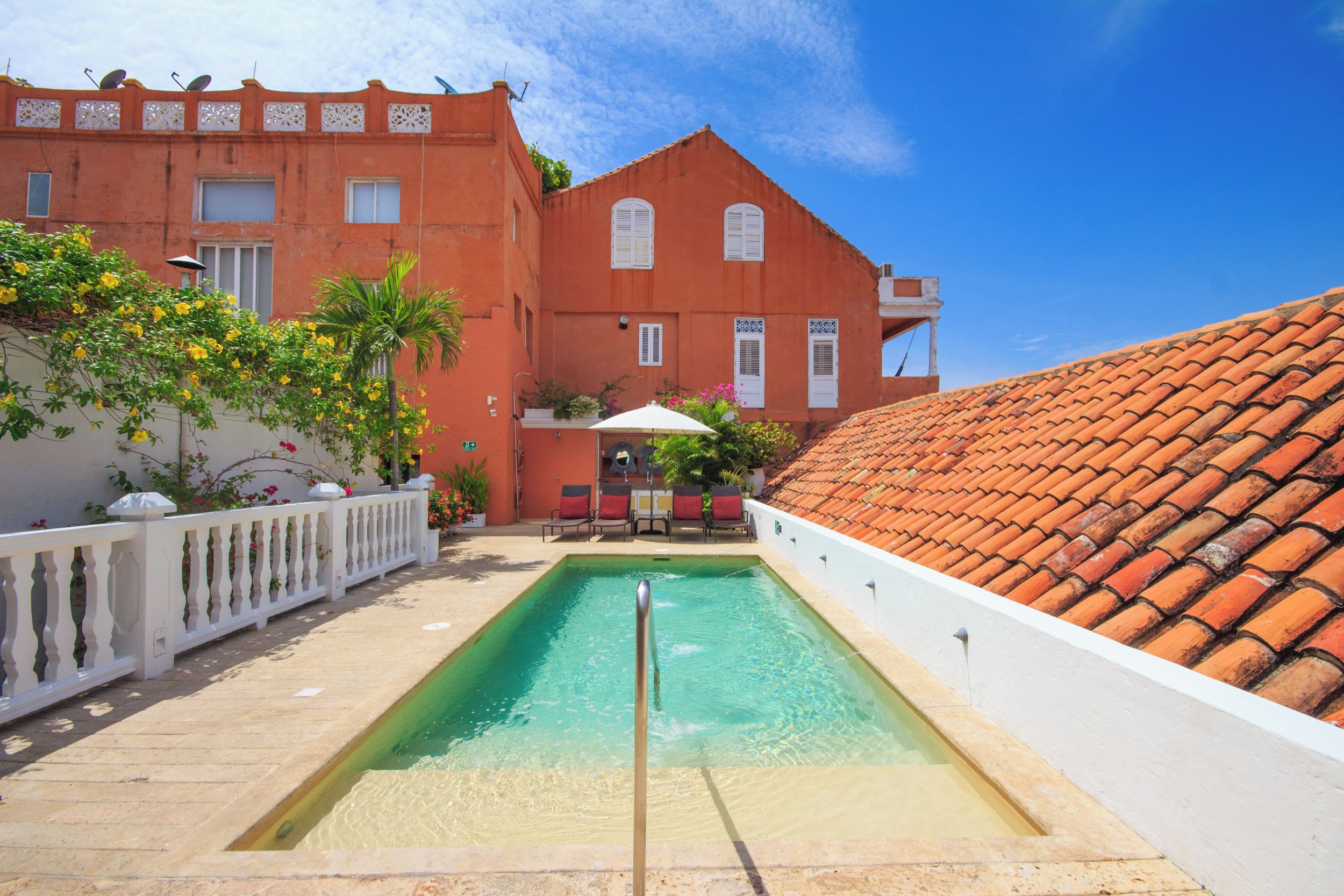 Una piscina con valla blanca, techo de tejas rojas y un edificio con balcones y ventanas.