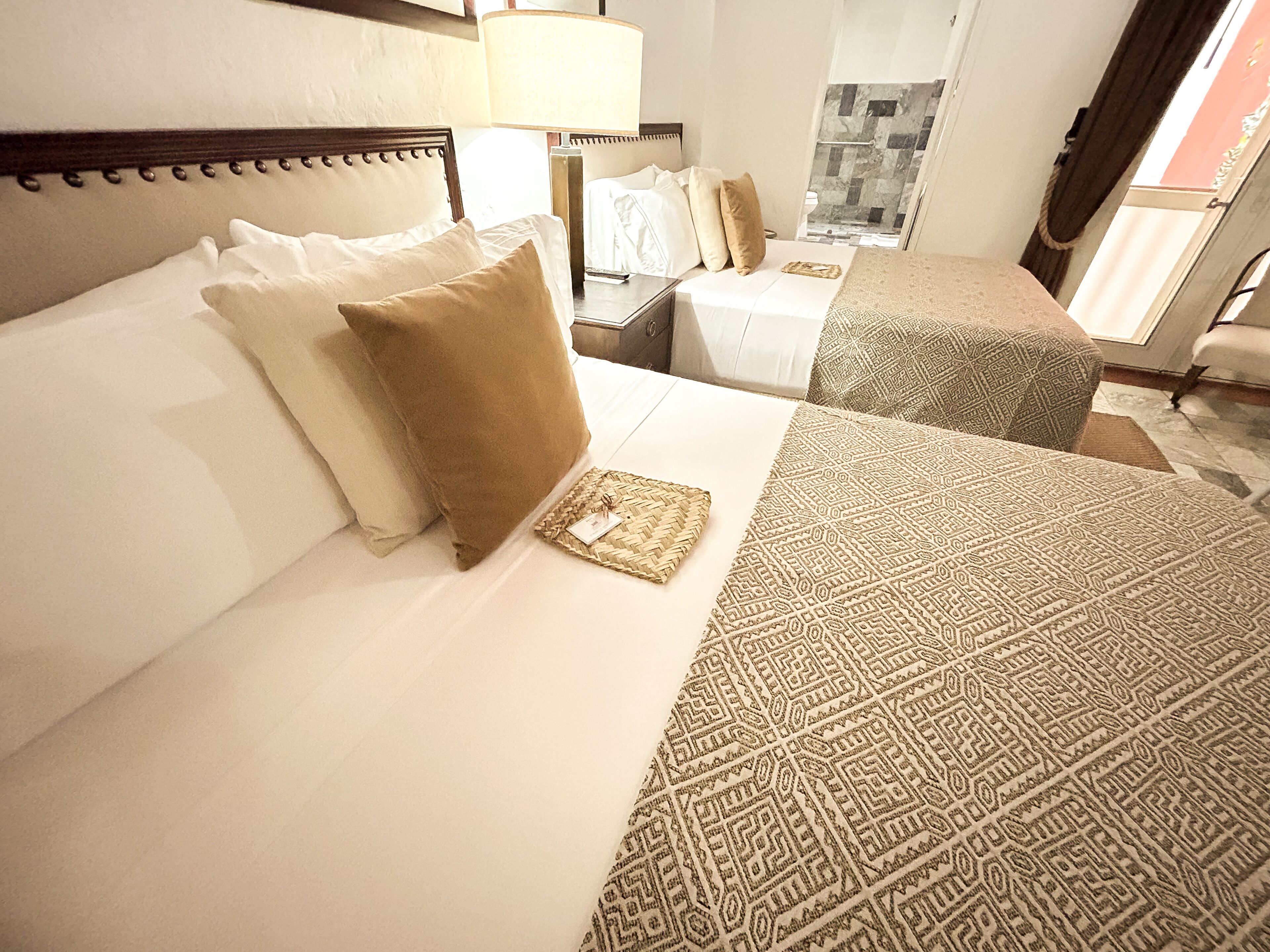 Una habitación de hotel con cama, mesita de noche, lámpara y zona de ducha.