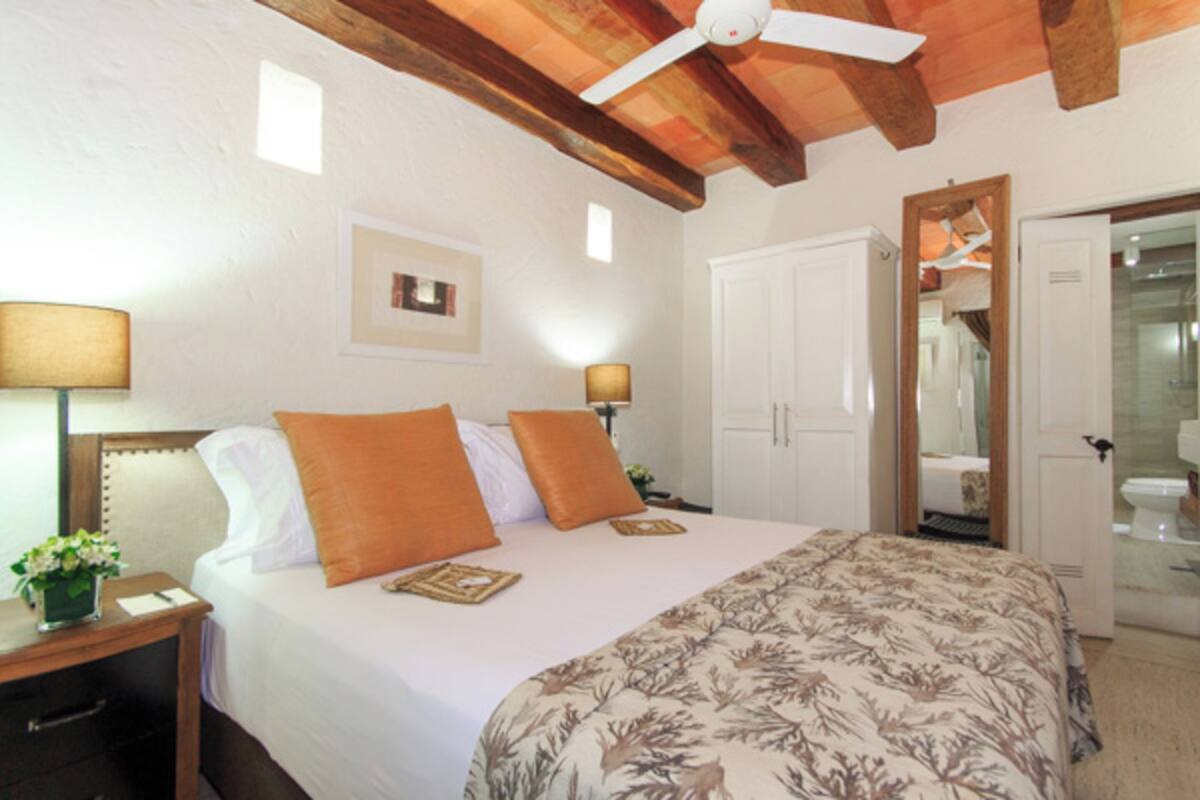 Une chambre à coucher comprenant un lit, deux tables de chevet, un ventilateur de plafond, une porte et un miroir.
