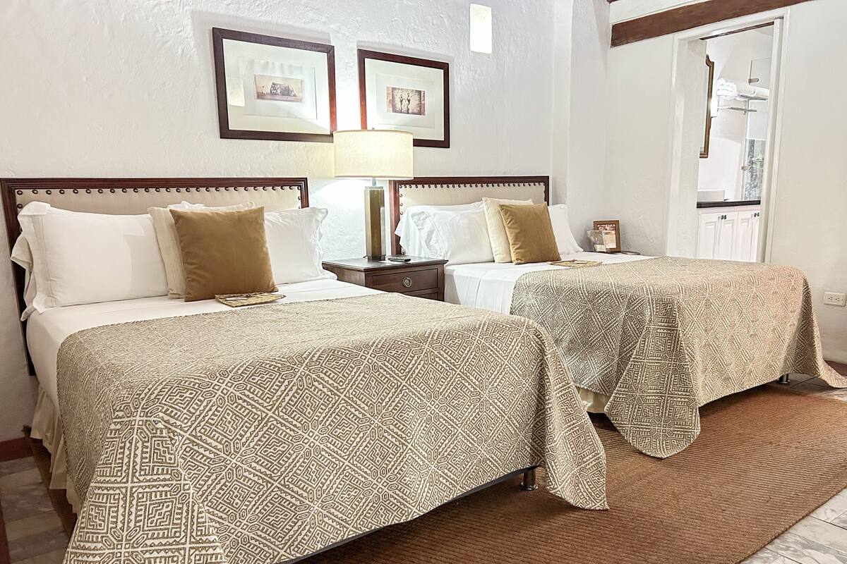 Une chambre d’hôtel avec deux lits, chacun recouvert d’une couvre-lit à motifs, une table de chevet avec une lampe et des tableaux encadrés accrochés au mur.