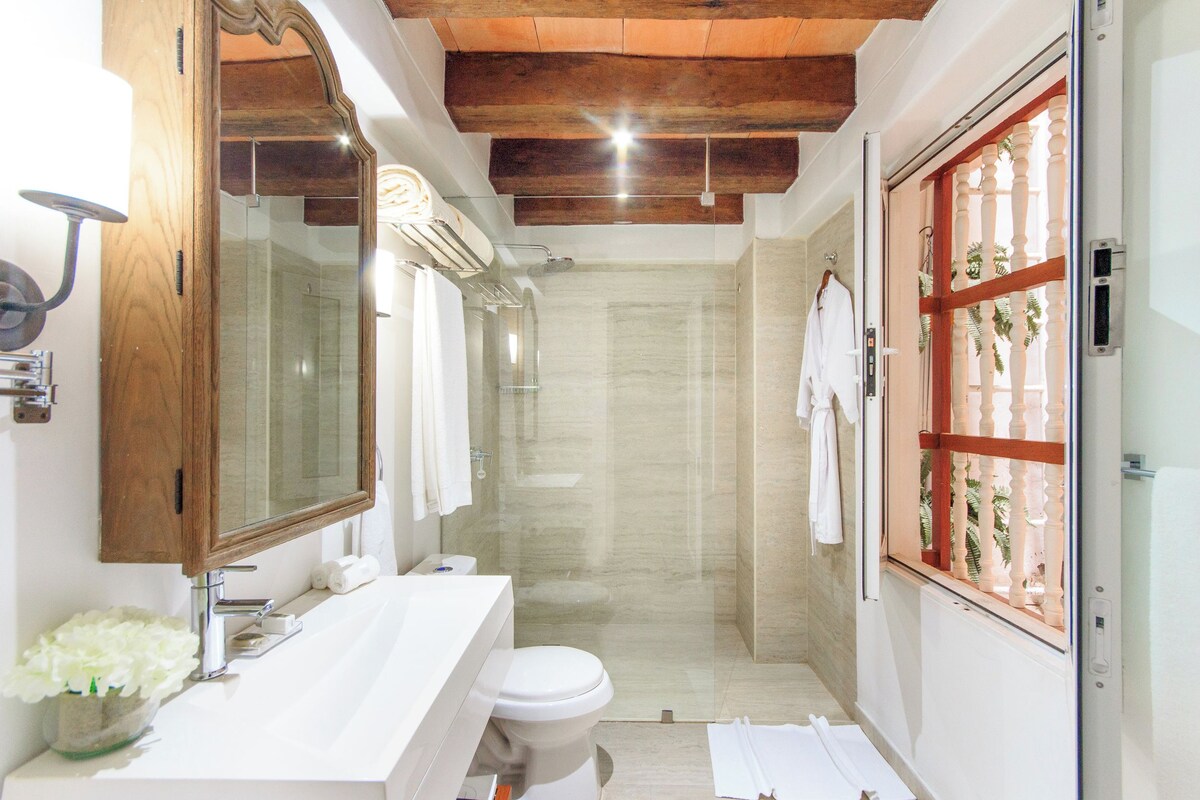 Une salle de bain avec un plafond en bois, une cabine de douche en verre, un lavabo blanc et un grand miroir.