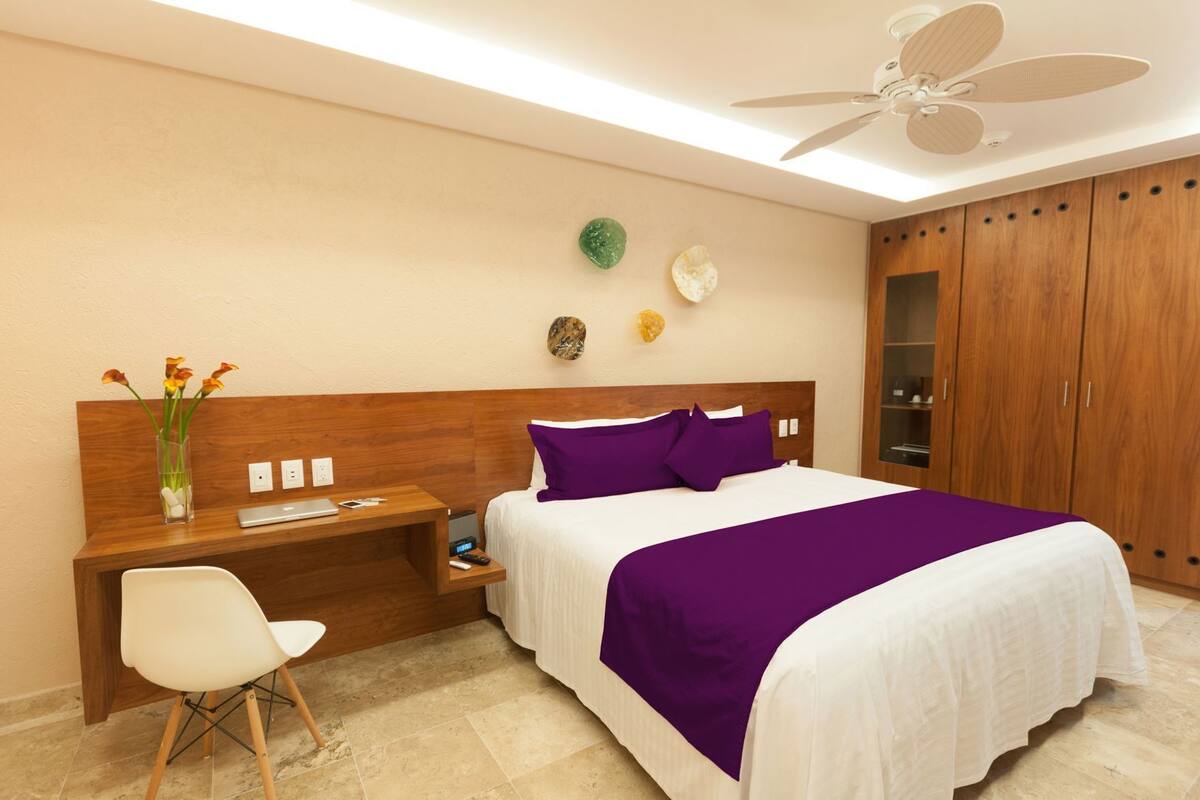 Ein Hotelzimmer mit Bett, Schreibtisch mit Stuhl, Nachttisch, Deckenventilator und Kleiderschrank.