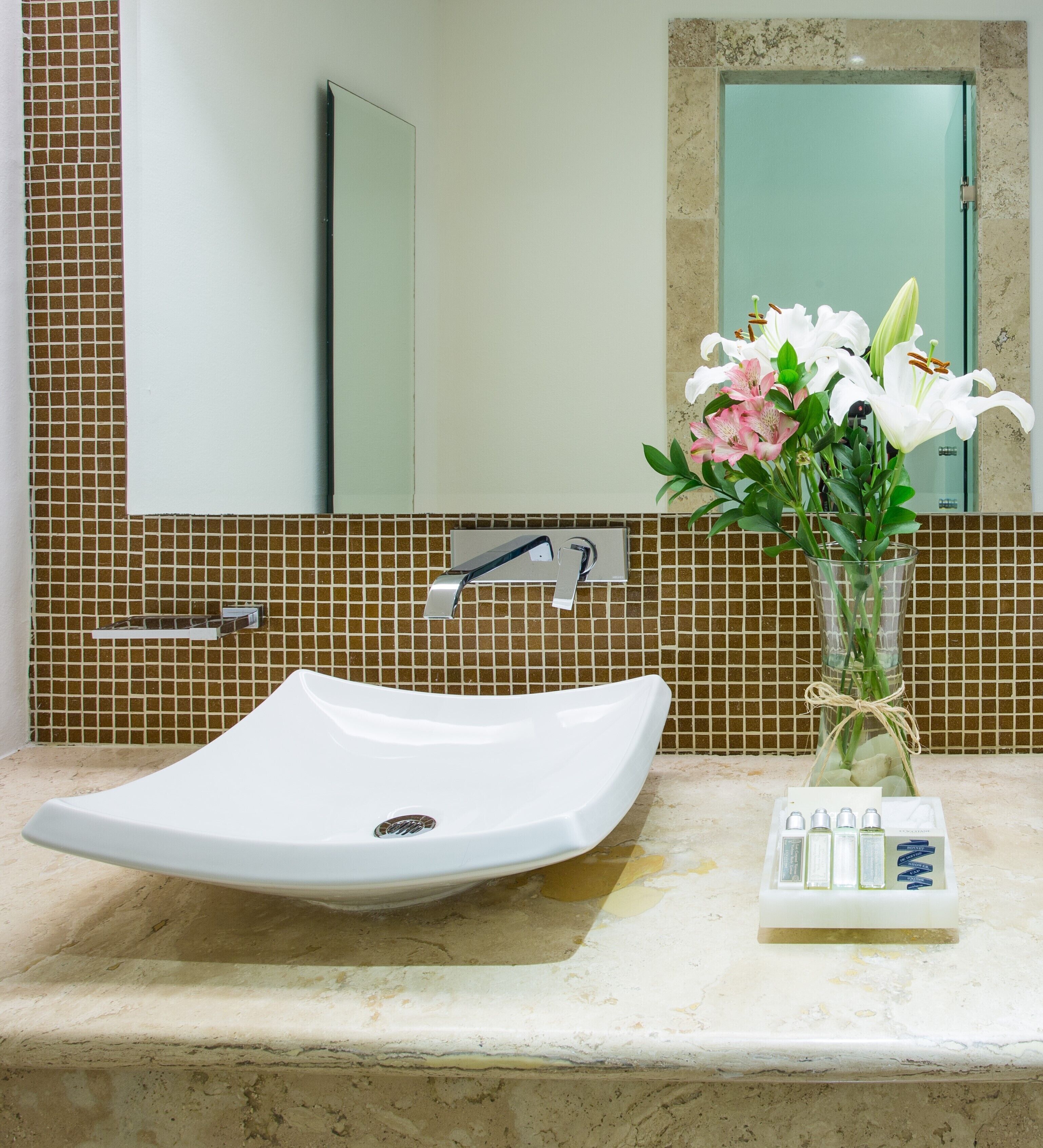 A bathroom with a white sink, a mirror, and a vase with flowers.