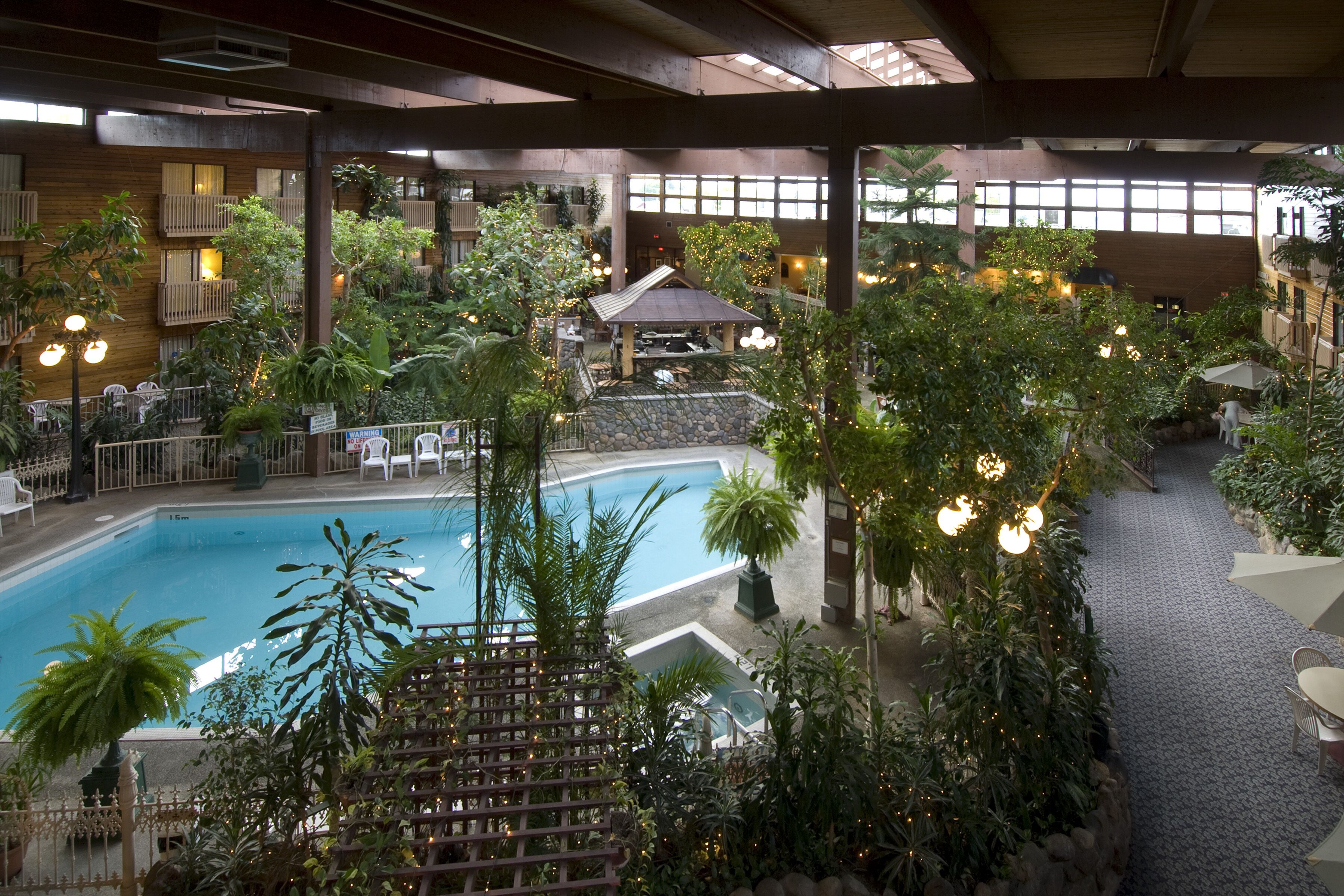Una piscina interior rodeada de exuberante vegetación, con varias zonas de estar y un pabellón cubierto.