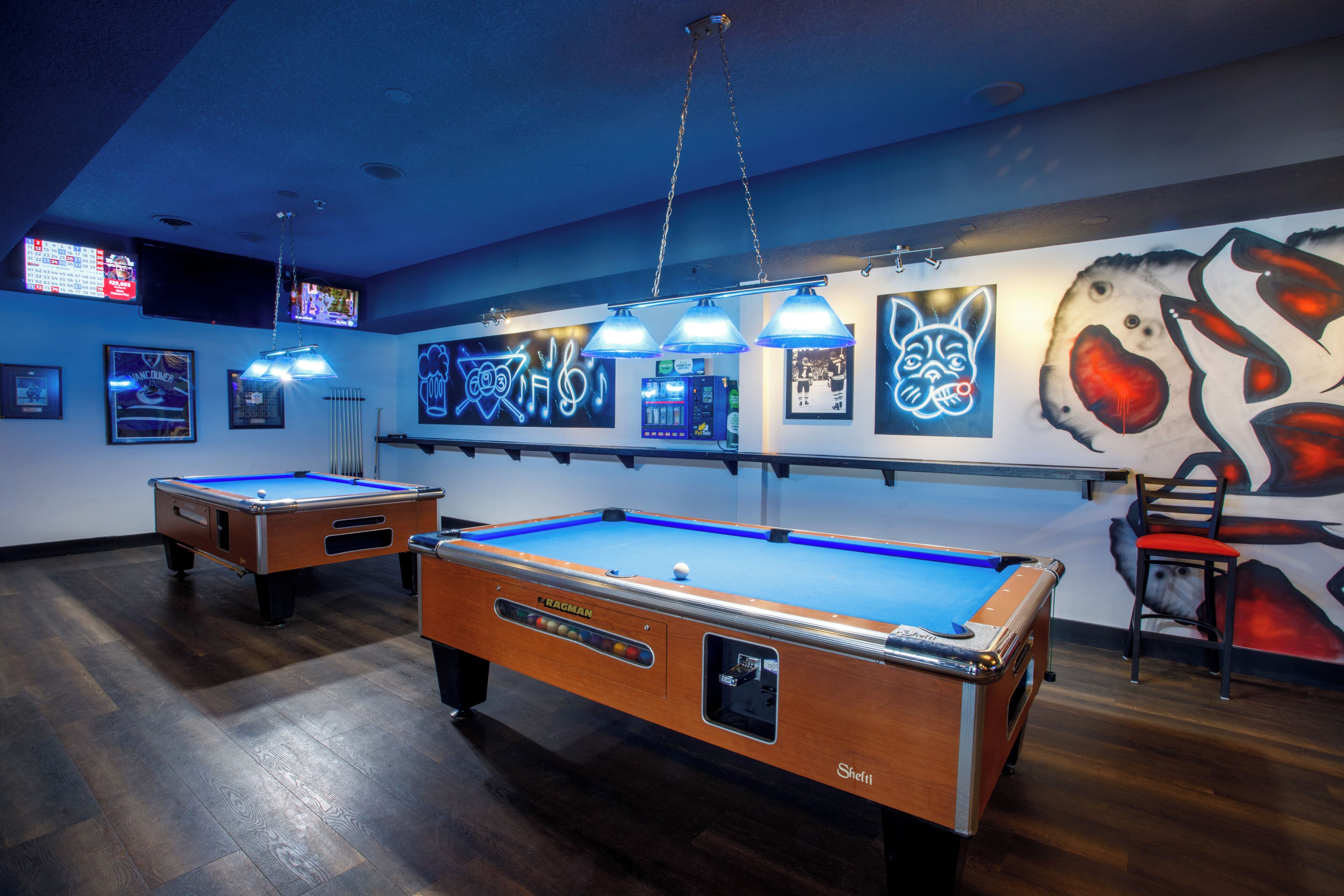 Een pooltafel met een neonbord, een stoel en een muur met kunstwerken.