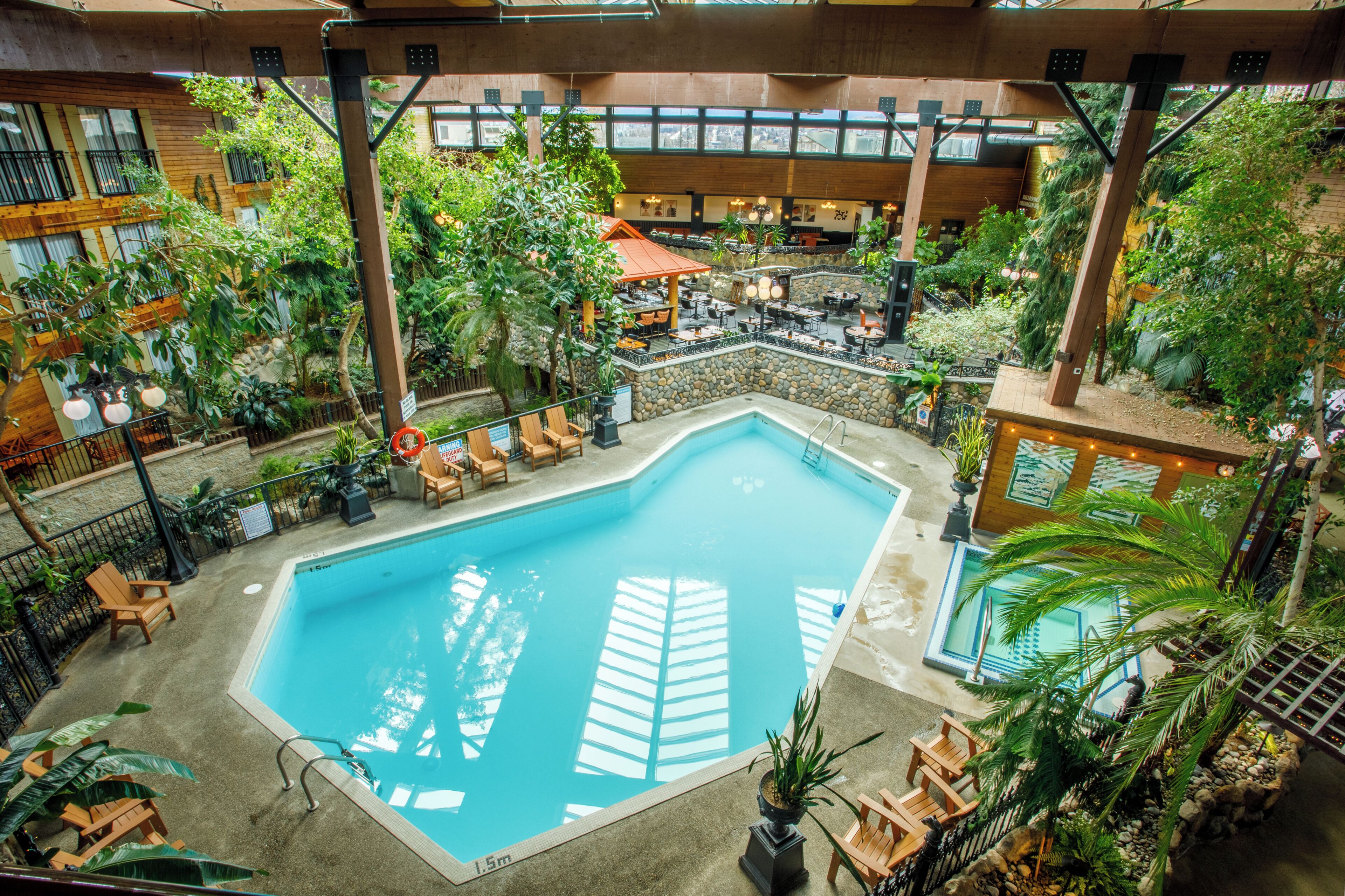 Piscina interior rodeada de asientos y follaje, con una zona de bar y una pared de piedra.