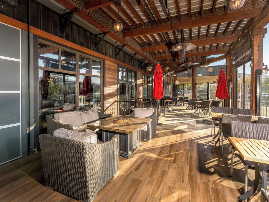 Un patio al aire libre con mobiliario de mimbre, mesas de madera y sombrillas rojas.