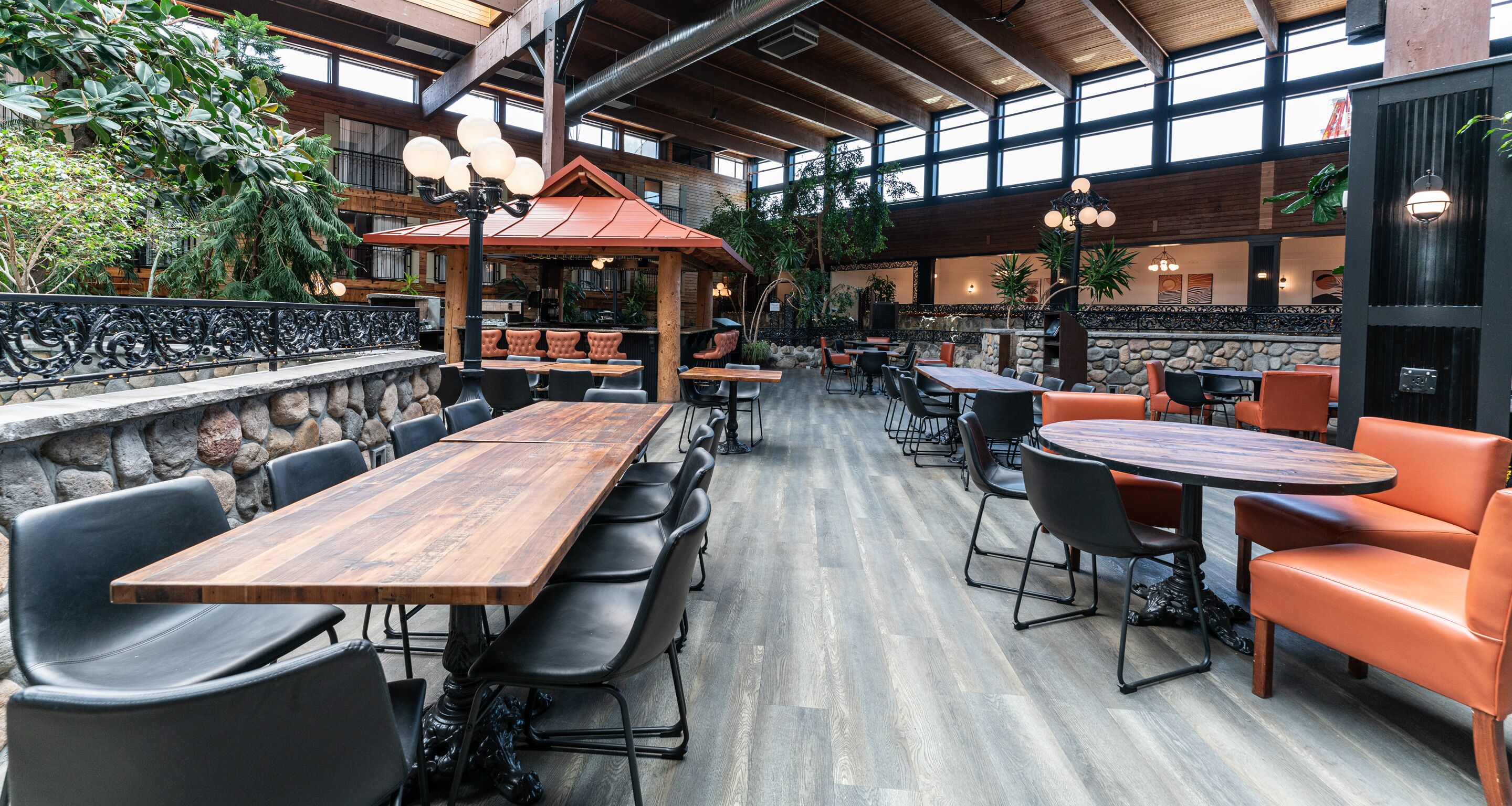 An indoor dining area with wooden tables and chairs, stone walls, and large windows.