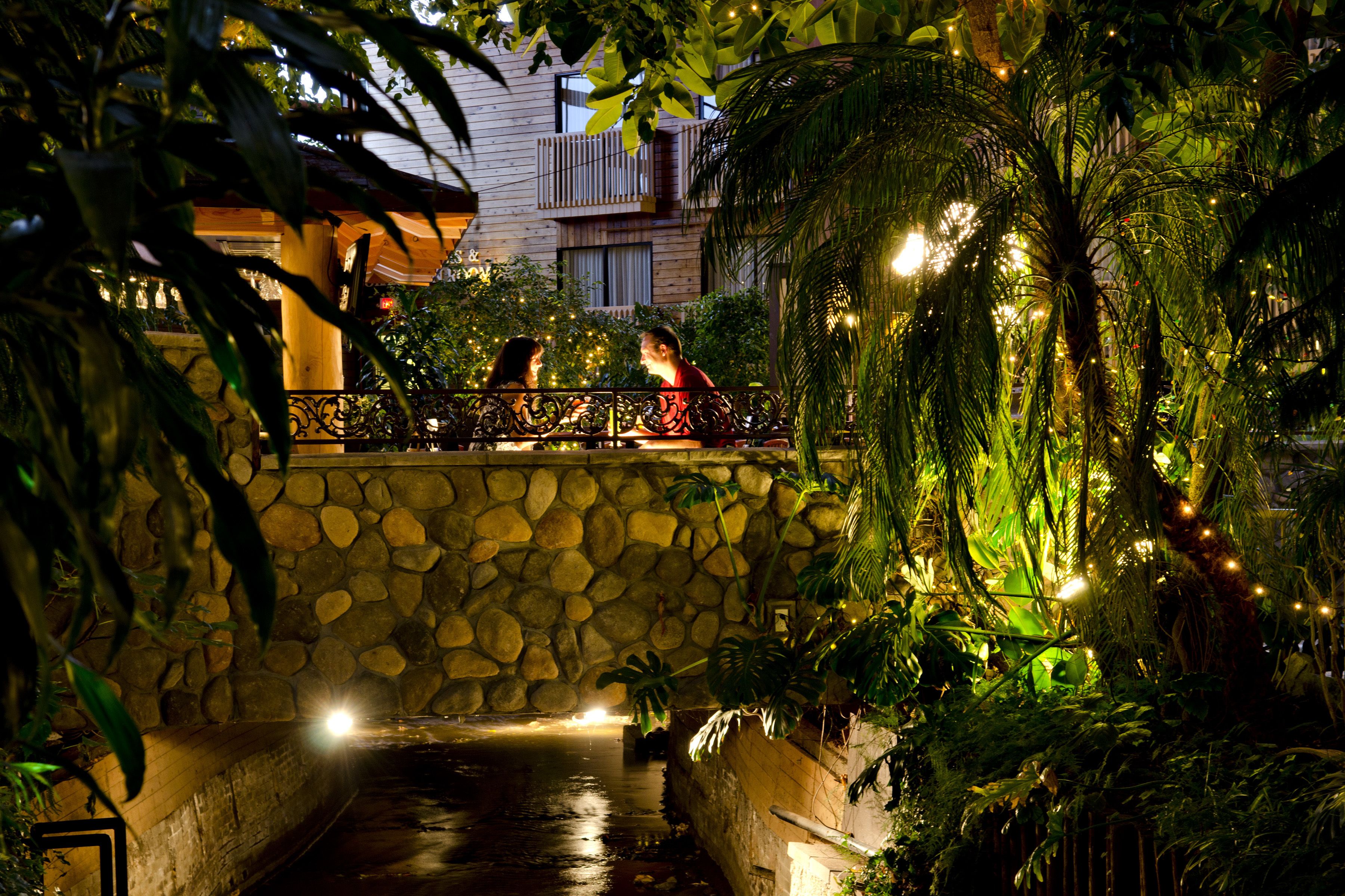 A stone bridge over a water channel, surrounded by lush greenery and decorative lights.