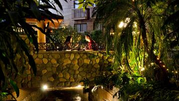 A stone bridge over a water channel, surrounded by lush greenery and decorative lights.