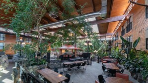 An indoor patio area with wooden tables and chairs, surrounded by stone walls and potted plants. - Prestige Vernon Lodge and Conference Centre (Vernon)