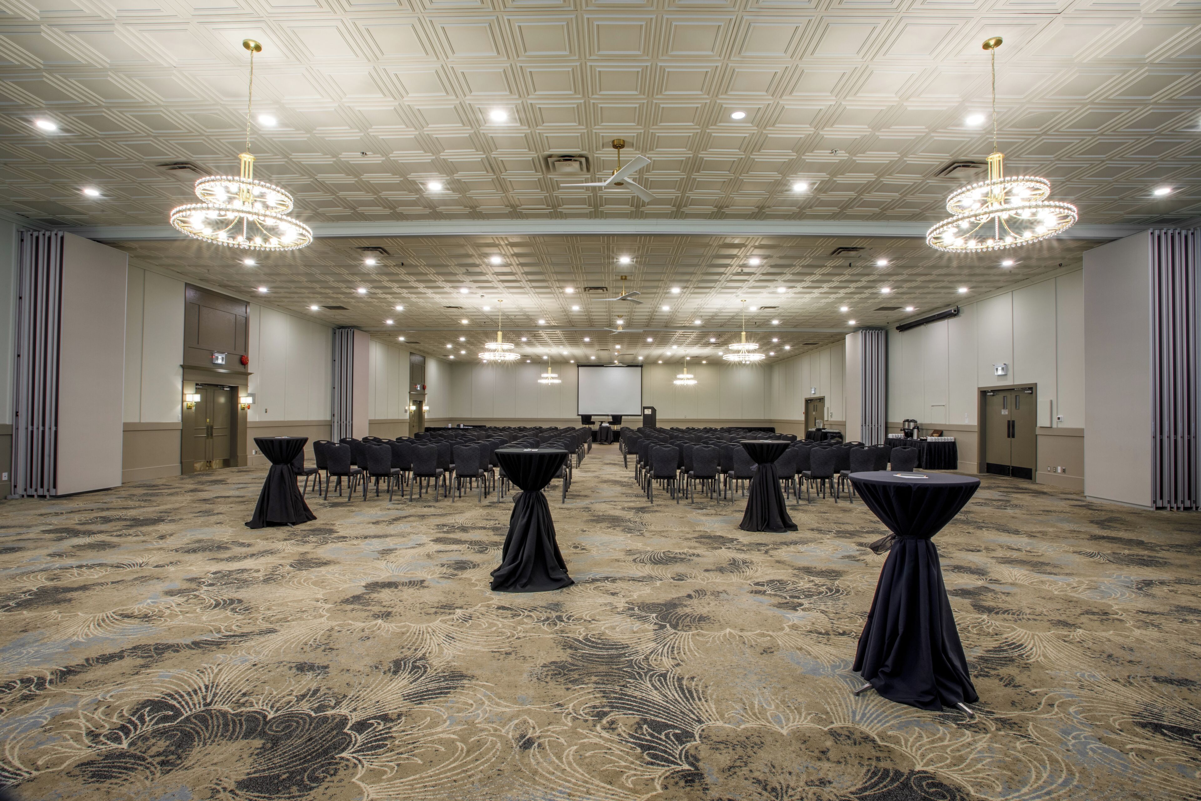 A conference room with a carpeted floor, tables with black tablecloths, and chandeliers.