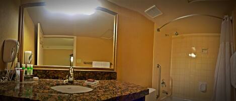 A bathroom with a granite countertop, a sink, a mirror, a shower with a grab bar, and a towel rack.