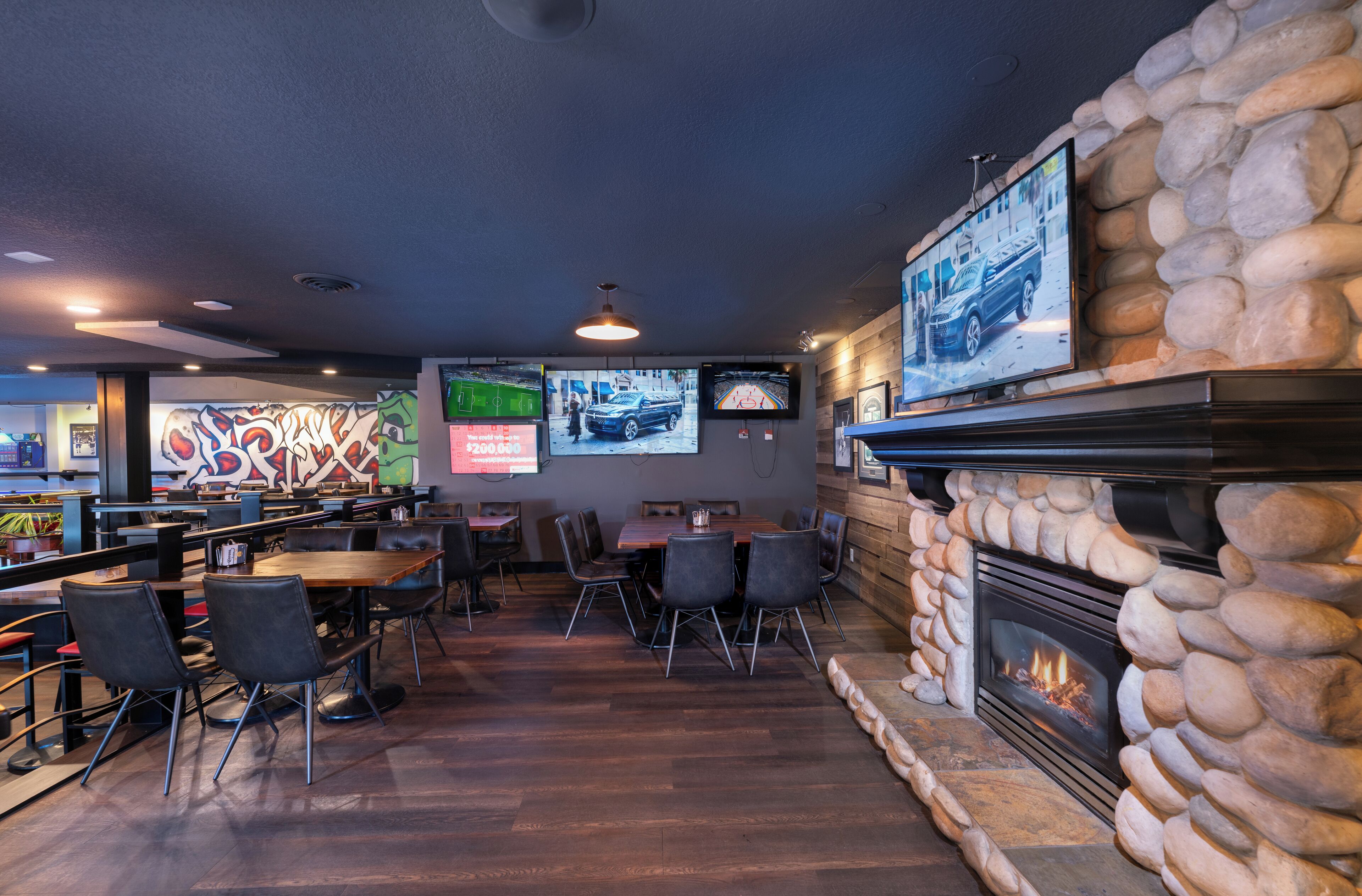 Un restaurant doté d’une cheminée en pierre, de plusieurs téléviseurs accrochés au mur et offrant différents types de sièges.