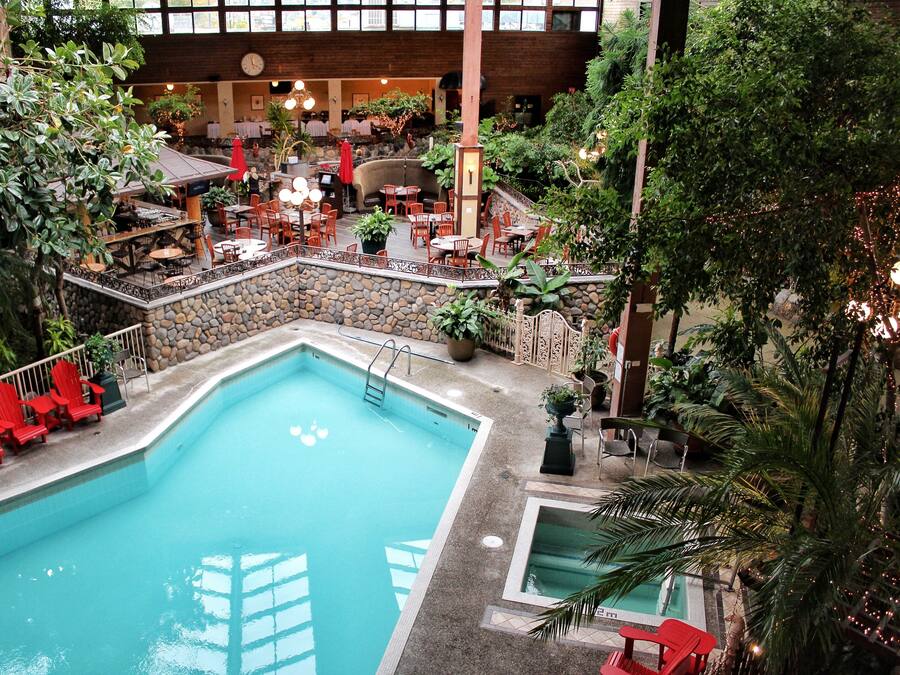 An indoor pool with red chairs and tables, surrounded by greenery and stone walls.