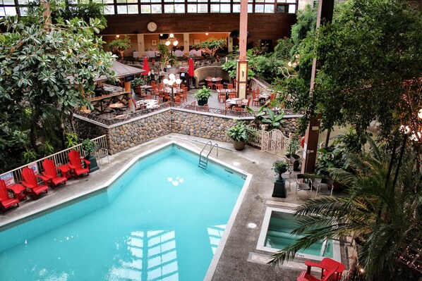An indoor pool with red chairs and tables, surrounded by greenery and stone walls.