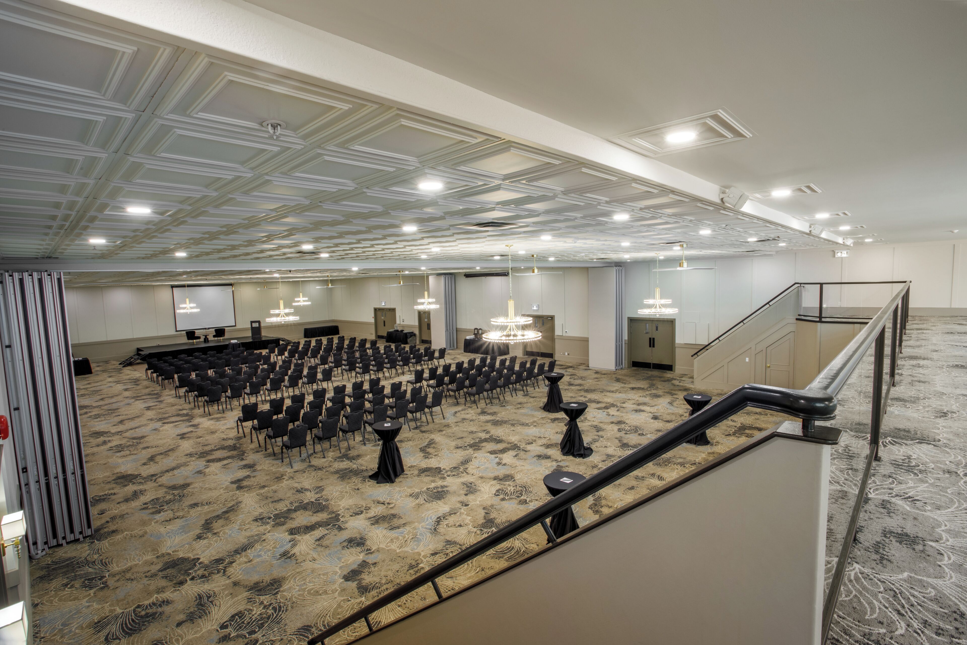 Un salón de conferencias amplio con filas de sillas, un escenario y una escalera que sube a un nivel superior.