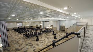 Un salón de conferencias amplio con filas de sillas, un escenario y una escalera que sube a un nivel superior.
